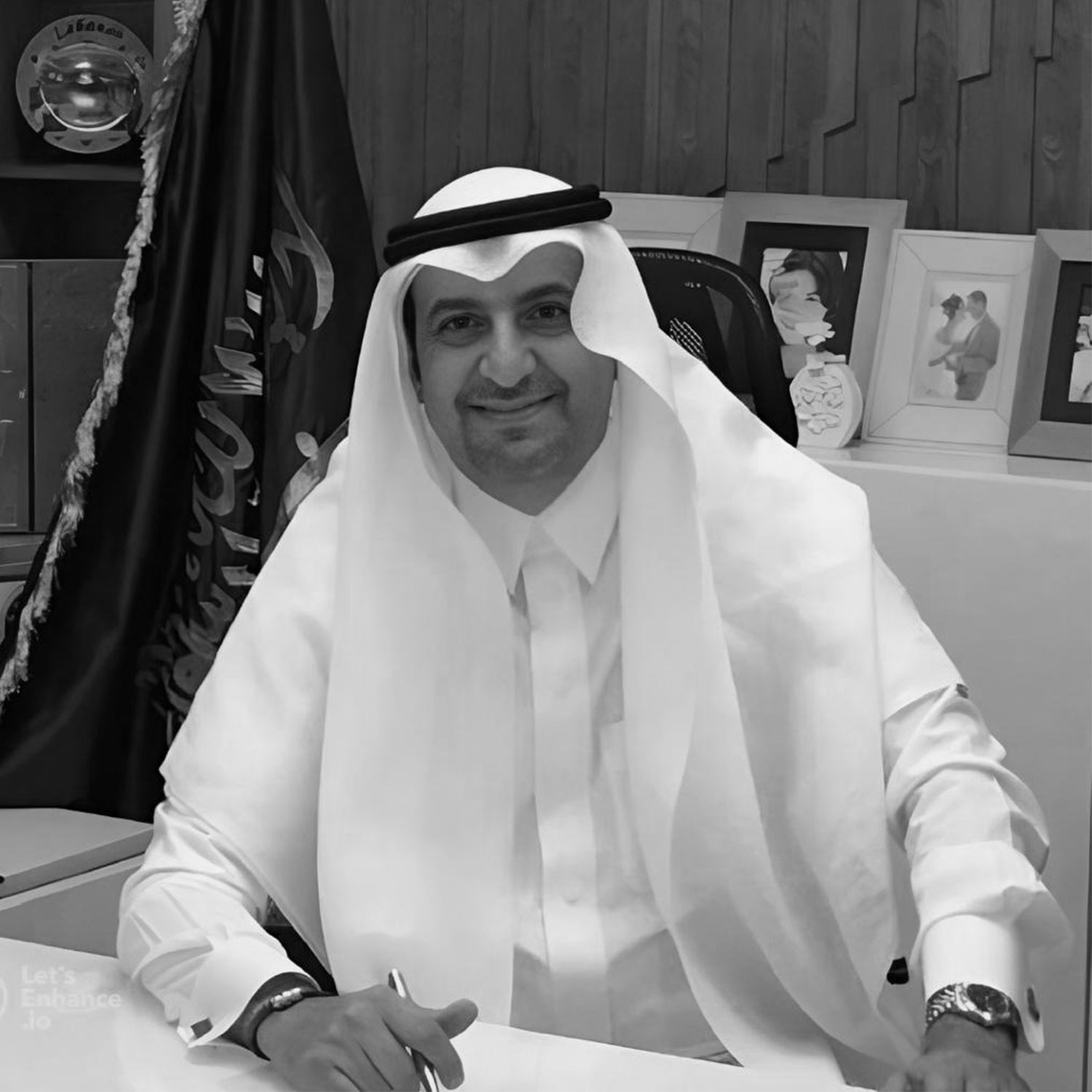 Man in traditional Arab attire smiles while signing a document at a desk in an office setting.